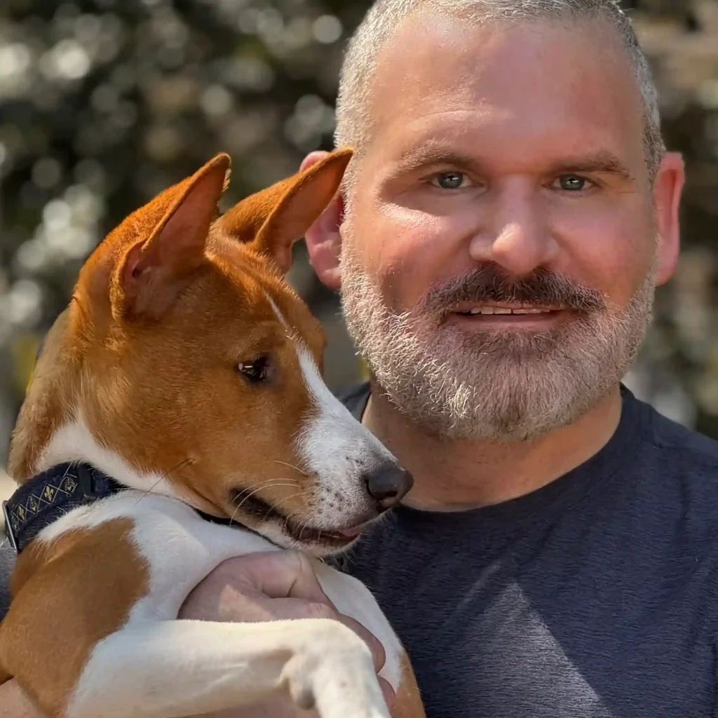 Therapist smiling outdoors while holding a friendly dog.